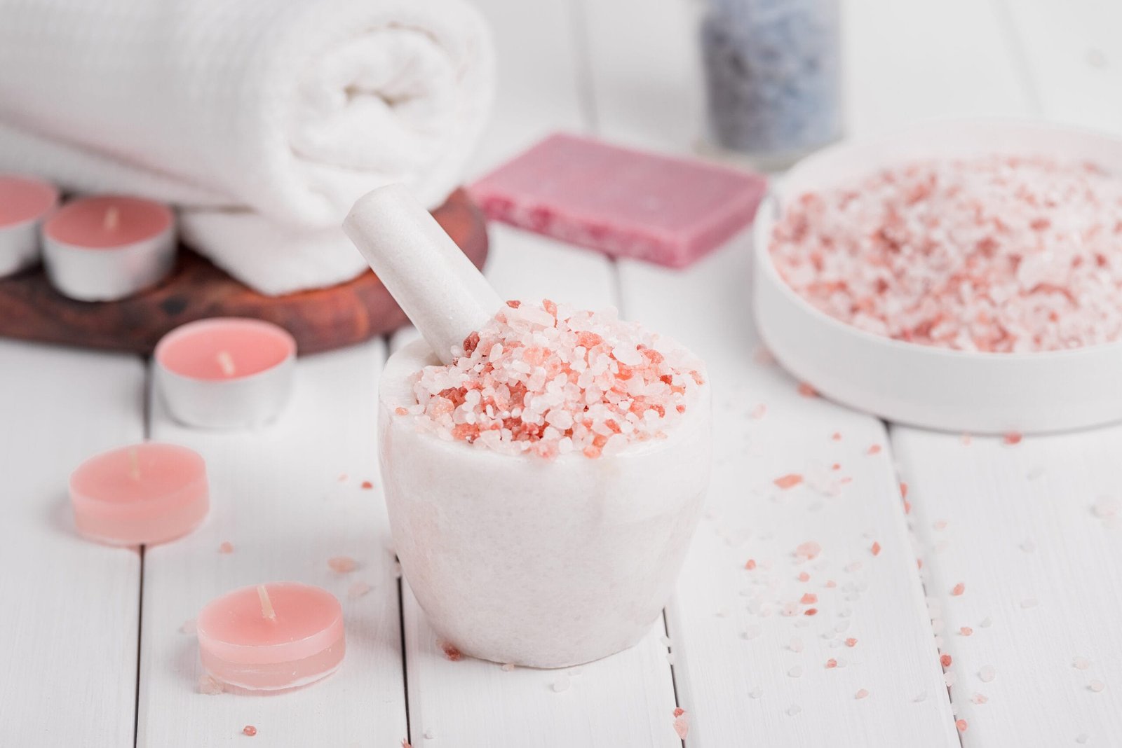 cleansing spa accessories with himalayan salt, rose soap petals and exfoliating bathroom products on distressed white wood background.