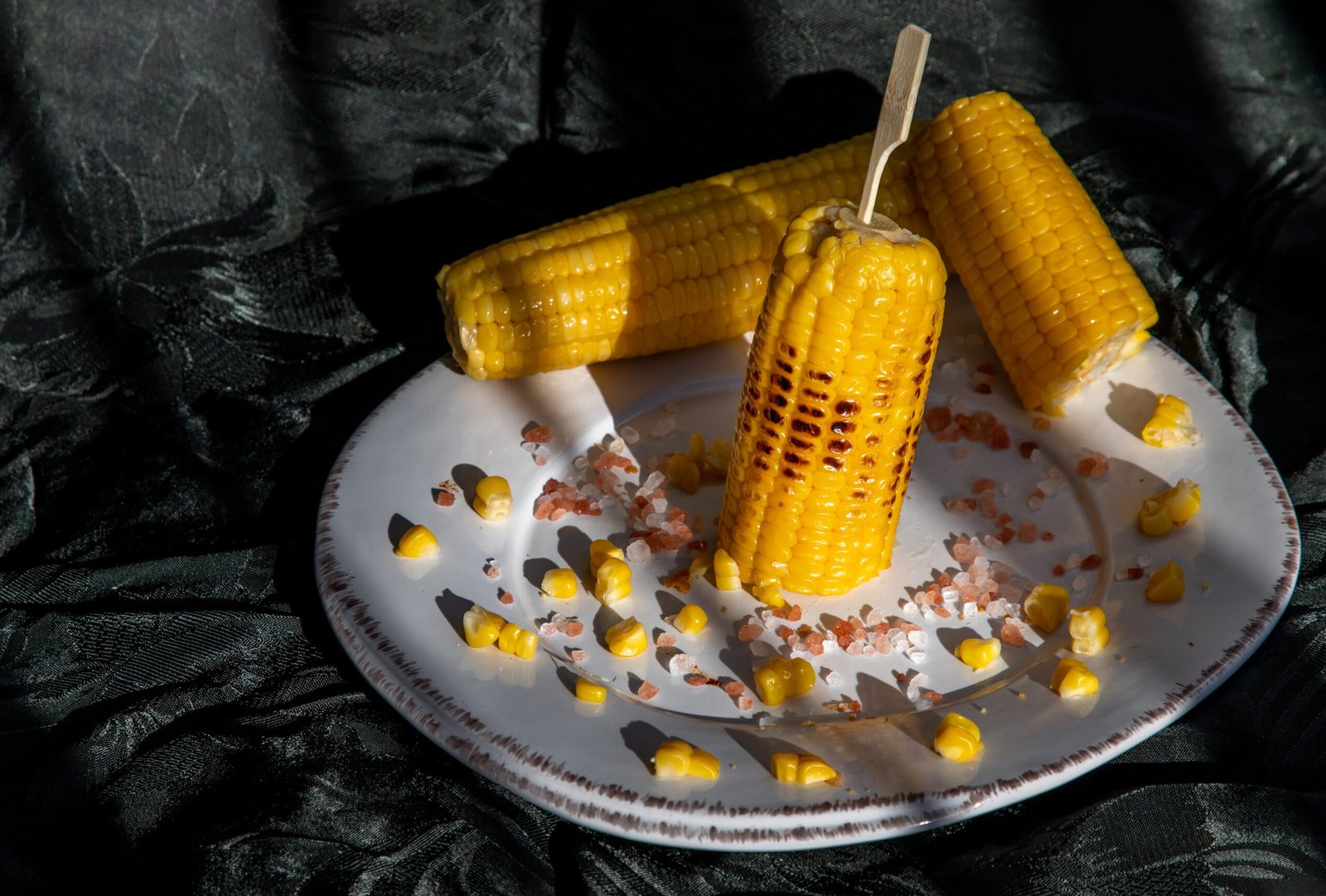 grilled corn on the cob on classic white plate over dark backgr